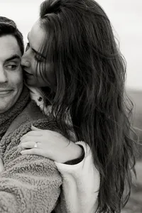A candid black and white photo of a couple whispering and snuggling close in the chilly mountain air during their engagement session in Boone, North Carolina, captured by North Carolina wedding photographer Jessica Leigh Mason.