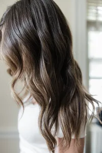 a brunette with medium length hair tilting her head toward the camera with brighter pieces framing her face