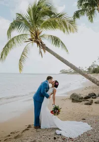 Man and wife kissing on a beach under a palm tree