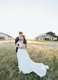 woman in a flowy white wedding dress held by her new husband in front of a white barn