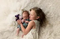 Sweet portrait of a big sister cuddling her newborn sibling while lying on a soft white rug, taken at Kara Reese Photography’s Waukesha studio serving Oconomowoc and New Berlin.