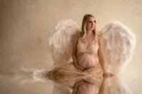 Blonde pregnant woman sits in angel wings and gold gown at our Waukesha County studio.