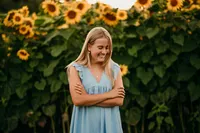A girl from Waukesha West High School stands in a Hartland, WI field of sunflowers wearing a denim sundress and looking at the ground in front of her.