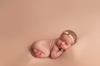 Peaceful newborn baby girl posed on a peach-colored blanket with floral headband during a minimalist newborn session near Waukesha, Brookfield, and Pewaukee.