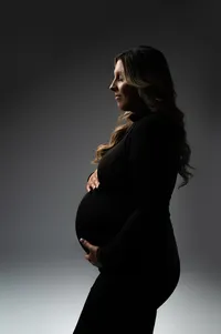 Elegant side profile of a pregnant woman in a black turtleneck, softly illuminated with moody directional lighting during a minimalist maternity session near New Berlin, Wisconsin.