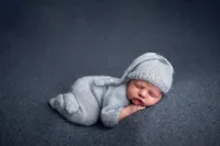 Sleeping newborn in light blue knit outfit and hat on dark blue backdrop, taken at a professional photo studio near Brookfield and Waukesha