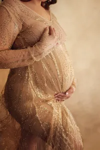 Close-up of a pregnant belly in a sparkling gold gown, hands gently cradling the bump in a glamorous and intimate maternity session near Pewaukee, Wisconsin.