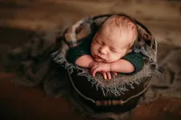 Newborn baby boy posed in a round bucket with a plaid blanket and green knit outfit, captured in warm earth tones by Kara Reese Photography near Pewaukee and Oconomowoc.