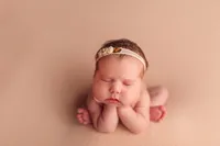 Iconic froggy pose of a newborn baby with soft peach tones and floral headband, photographed in a professional Lake Country photo studio.