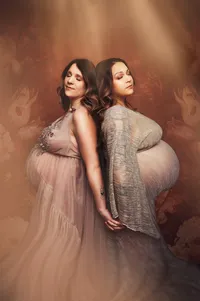 Pregnant twin women lean into each other, wearing gowns from our client closet.