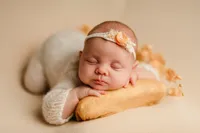 Close-up newborn photo of a baby girl posed on a peachy blanket in a cream knit outfit, wearing a delicate orange headband, during a professional session in Waukesha, Wisconsin.