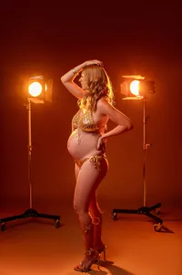 Pregnant woman posing confidently in a gold bikini and high heels, illuminated by studio lights for a bold, fashion-inspired maternity portrait in Waukesha, Wisconsin.