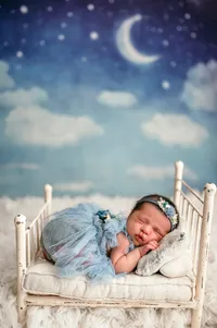 Newborn baby girl wearing a blue tulle dress sleeps peacefully on a vintage mini bed with moon and stars backdrop in a Waukesha, WI photography studio.
