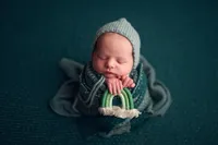 Newborn baby boy wrapped in green and holding a mini rainbow prop, photographed on a textured green backdrop at Kara Reese Photography, serving Waukesha and Brookfield.