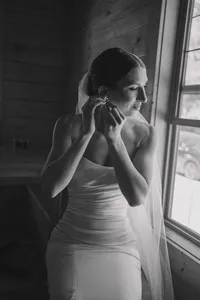 bride sitting in front of a windor putting on her earrings