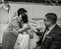Bride hugging the mother of the groom, as the groom looks on with a smile.