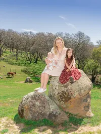 Orange County family photography of a mother and her two daughters sitting on a rock in a happy candid moment with true to life color and soft natural light.