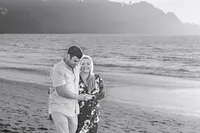 Black and white engagement photo of a couple walking toward the camera on the beach at sunset.