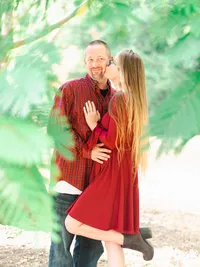Couple wearing red outfits during a Christmas engagement photo session in a Los Angeles park with festive holiday vibes.