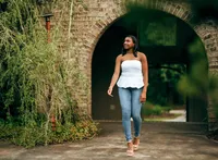 Senior portrait at Bella Sera Gardens in Loxley, Alabama — holding her necklace with one hand,
the other hand above her head, archway behind her.