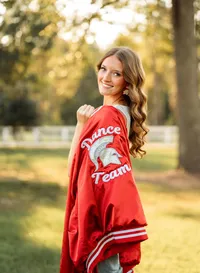 Senior portrait in downtown Magnolia Springs, Alabama — looking back at the camera with her dance team jacket draped over her shoulder.
