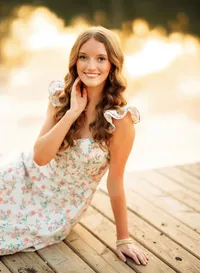 Senior portrait in downtown Magnolia Springs, Alabama — touching her face in a flowery dress.