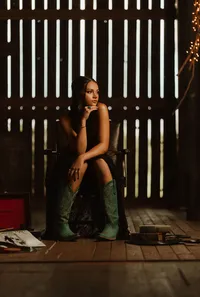 Senior portrait at Triple T Farms in Fruitdale, Alabama — sitting in a leather chair in an elegant
black dress and teal cowboy boots.