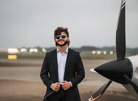 Senior portrait at a small hangar near Mobile International Airport in Mobile, Alabama — suit
jacket over his shoulder, wearing aviators with the plane in the background.