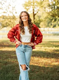 Senior portrait in downtown Magnolia Springs, Alabama — having a laugh in her dance team jacket hands on hips.