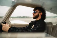 Senior portrait at a small hangar near Mobile International Airport in Mobile, Alabama — sitting
in the cockpit holding the yoke, wearing aviators.