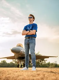 Senior portrait at Battleship Memorial Park in Mobile, Alabama— low angle with arms crossed with a sunset and an f-16 fighter jet in the background.