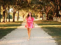 Senior portrait in downtown Magnolia Springs, Alabama — walking down a white gravel road wearing a bright pink outfit.