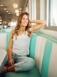 Senior portrait at Sunliner Diner in Gulf Shores, Alabama — sitting in a booth, laughing with her
hand in her hair.
