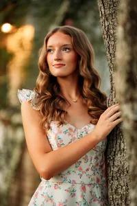 Senior portrait in downtown Magnolia Springs, Alabama — leaning against a tree in her flowery dress.