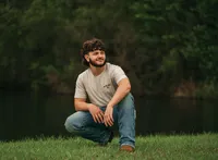 Senior portrait at Circle B Lake in Wilmer, Alabama — crouching in the grass with a pond and
greenery in the background.