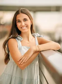 Senior portrait at The Wharf in Orange Beach, Alabama — leaning on a railing in a white-and-
blue striped dress, bridge behind her.