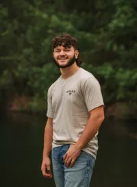 Senior portrait at Circle B Lake in Wilmer, Alabama — standing in jeans with a thumb in his
pocket, pond in the background.