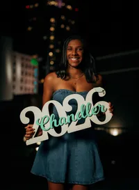 Senior portrait in downtown Mobile, Alabama — holding a white wooden “2026” sign for her
class year.