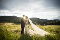 Bride and groom share a quiet moment in a Colorado meadow at sunset, her cathedral veil trailing across the grass.