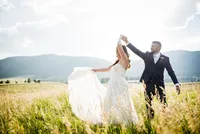 A groom twirls his bride in a Colorado mountain meadow, her lace gown flaring in the wind.
