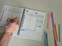 Hand writing inside the Time Magic Planner during a weekly planning session with colorful pens.