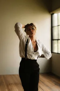 Editorial style portrait of a woman in natural window light, dressed in a white linen shirt and black skirt, captured in a minimal studio with warm, moody tones.