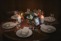 Table de réception en bois foncé avec bougies, centre de table floral coloré et cadre photo, menus et couverts dorés, ambiance intime et chaleureuse au Centre des Sciences de Montréal