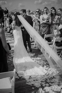 Mariée remontant l'allée au bras de son père, longue traîne de dentelle et pétales de fleurs au sol, invités assis de chaque côté, cérémonie au Belvédère du Vieux-Port de Montréal