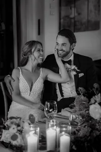 Mariés riant à table lors du cocktail, la mariée touchant le visage du marié avec tendresse, ambiance chaleureuse en noir et blanc au terrain de golf de Saint-Lambert