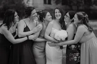 Mariée souriante entourée de ses demoiselles d'honneur, rires et étreintes complices, bouquet blanc en main, portrait de groupe au Vieux-Port de Montréal