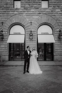 Mariés posant élégamment devant une façade historique aux arches jumelles, robe vaporeuse et complet noir, ambiance urbaine italienne en noir et blanc