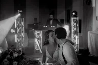 Mariés partageant un baiser tendre à leur table de réception, sous les lumières de la soirée, DJ en arrière-plan — instant authentique capturé par un photographe de mariage à Montréal, illustrant l’émotion et l’atmosphère festive de la célébration.