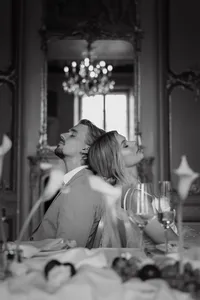Couple dos à dos, yeux fermés, dans un salon élégant orné d'un lustre à pampilles et de miroirs dorés, portrait éditorial en noir et blanc
