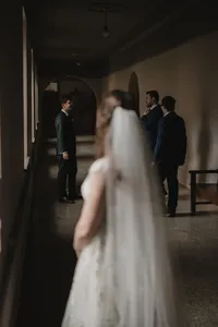 Mariée floue au premier plan sous son voile, marié et garçons d'honneur discrets dans un corridor voûté, moment de first look à l'Auberge Willow Inn, Hudson
